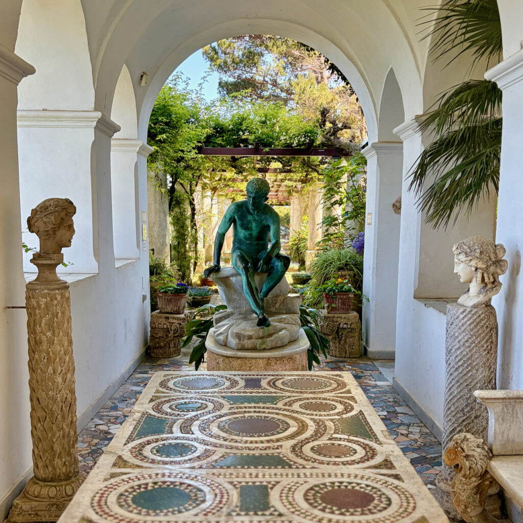View through an arched garden passage at Villa San Michele with a patinated metal statue, mosaic floor, and surrounding plants