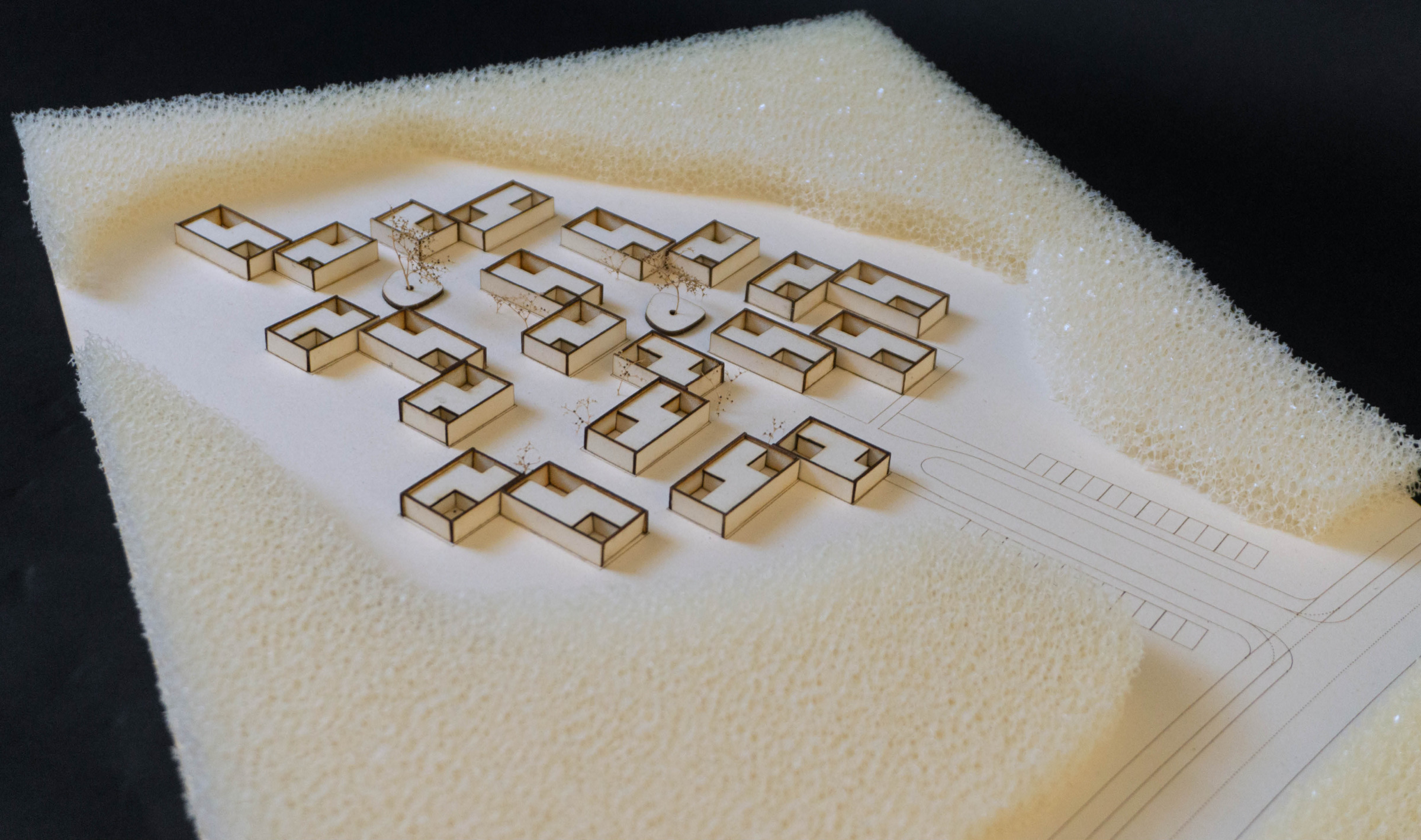 Physical site model showing the housing cluster arranged within a pale landscape base.