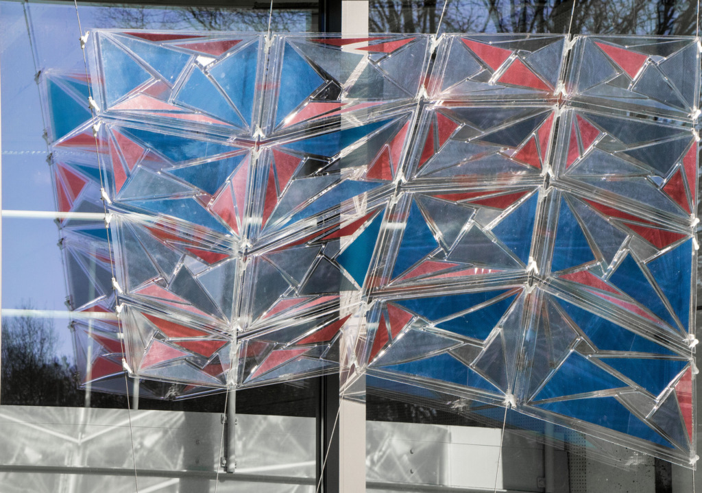Close view of a transparent Adaptive Sun Skins facade demonstrator with folded polycarbonate panels and colored OPV surfaces.