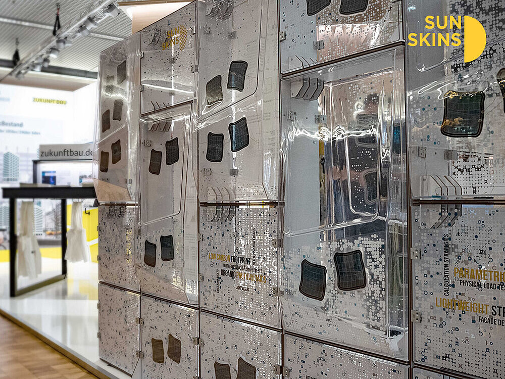 Exhibition view of the Adaptive Sun Skins demonstrator with transparent panels, printed patterns, and integrated OPV modules.
