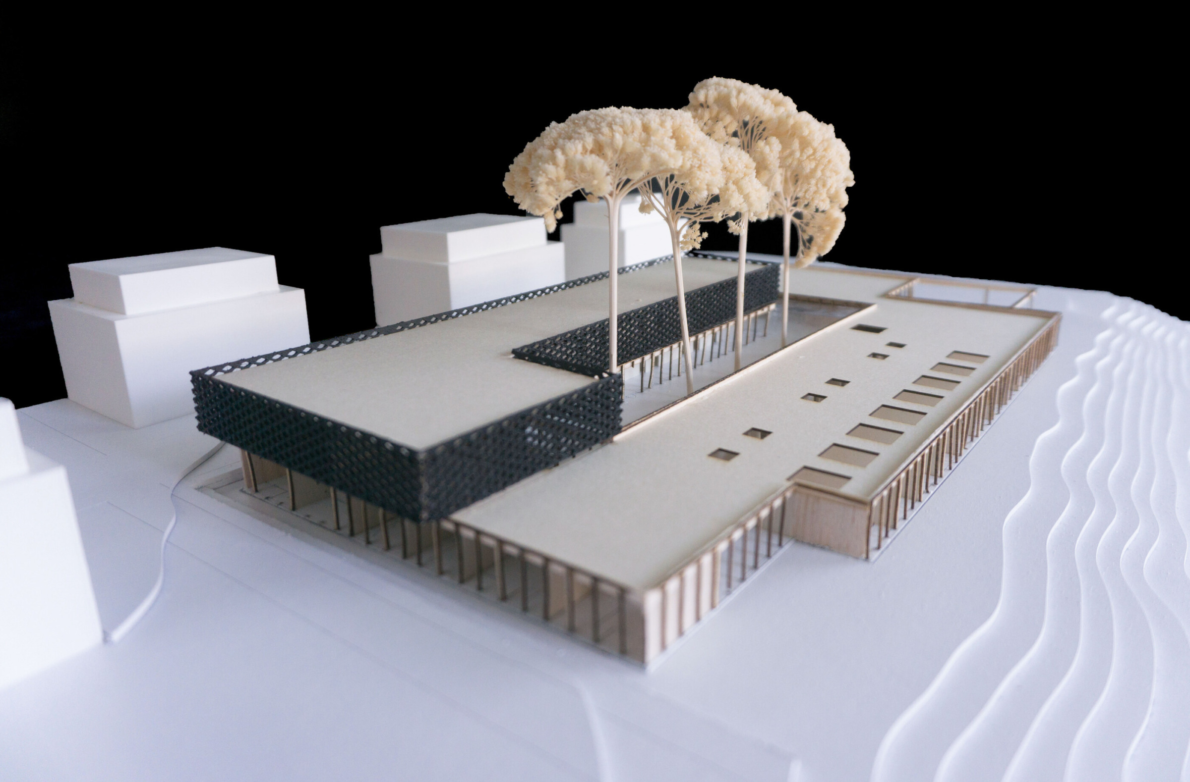 Physical model detail view of the dark faceted upper envelope, timber ground floor and courtyard edge.